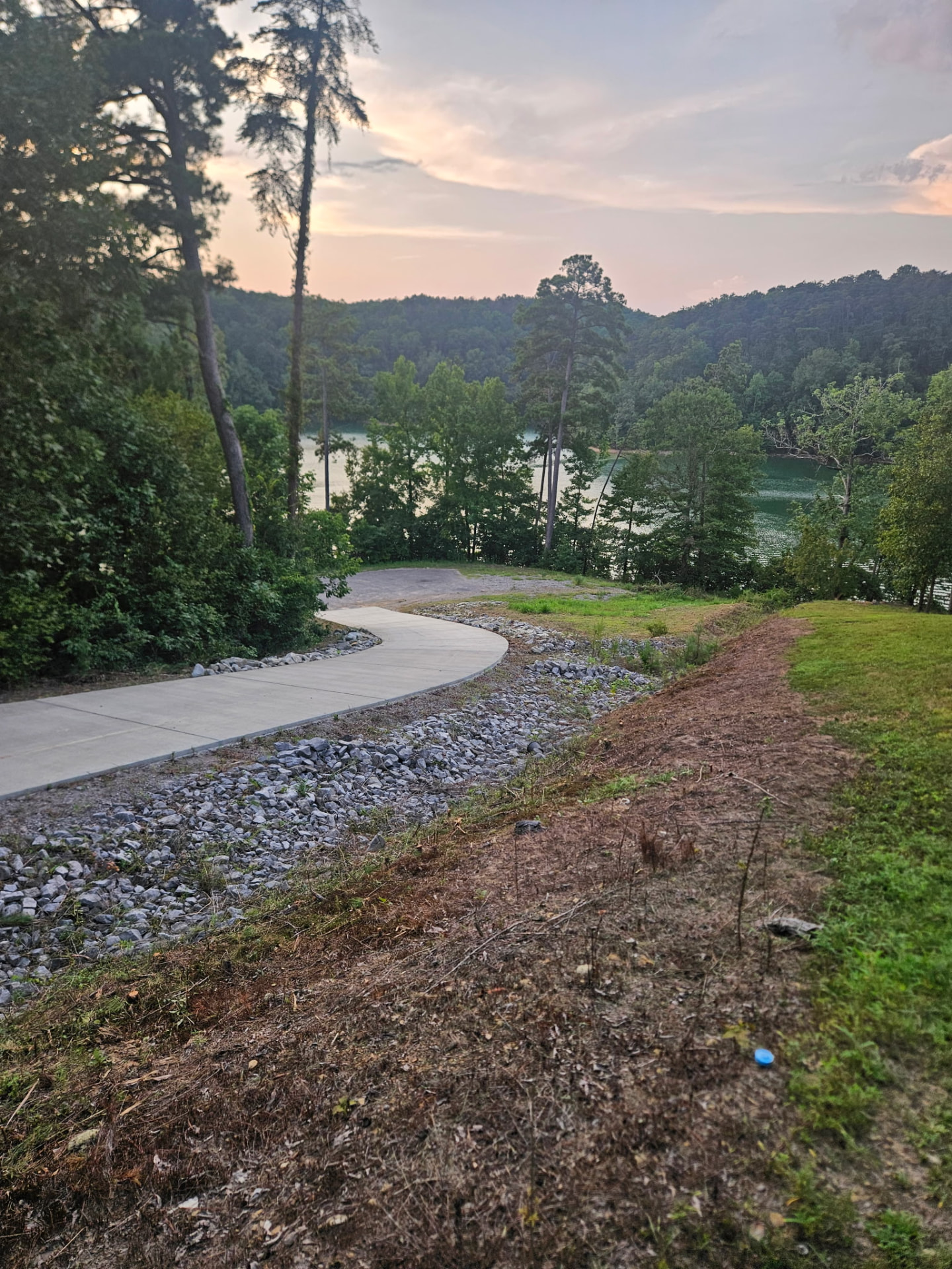 New paved walkway leading toward the lake at sunset with forested hills in the background